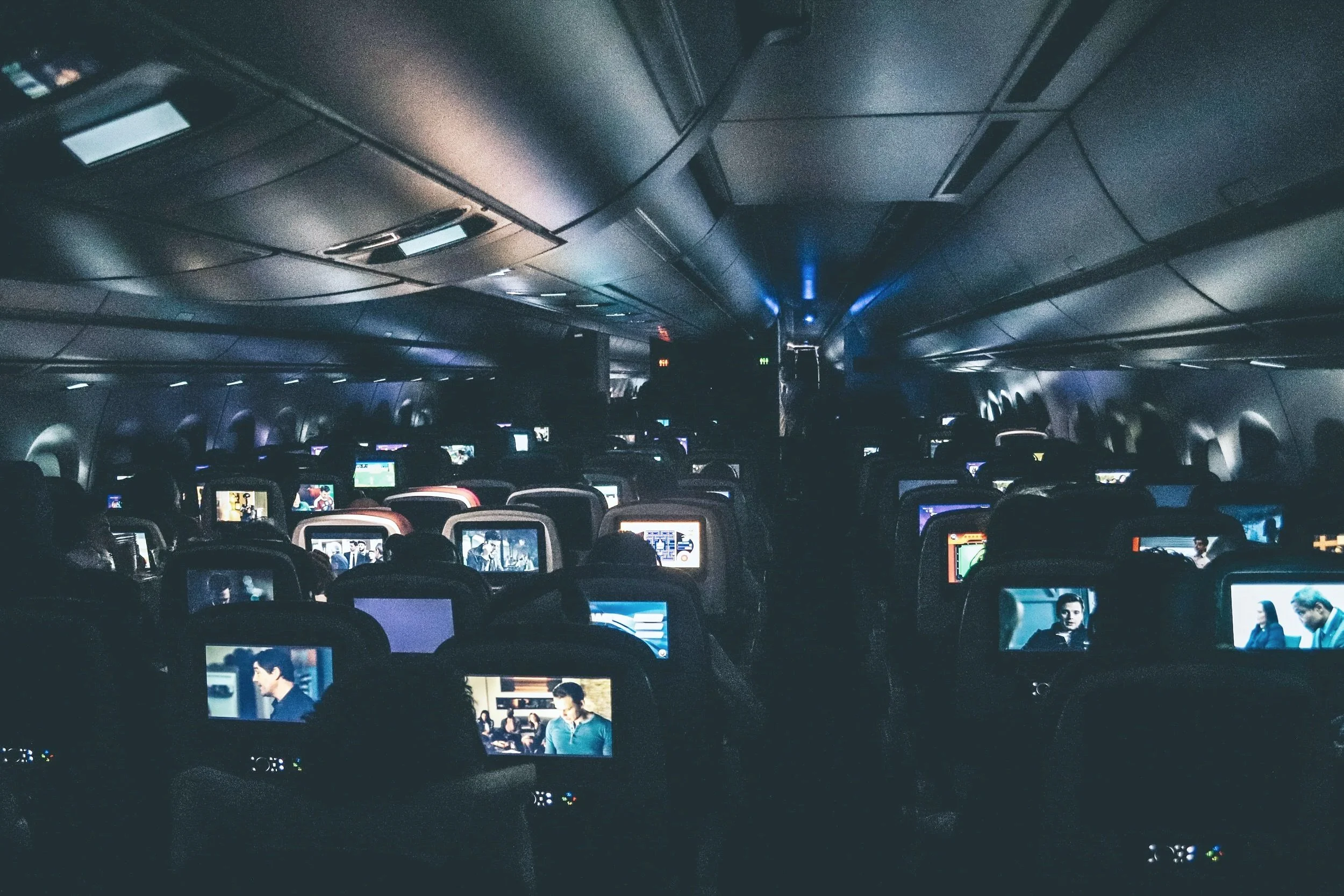 A dark plane full of passengers watching movies.