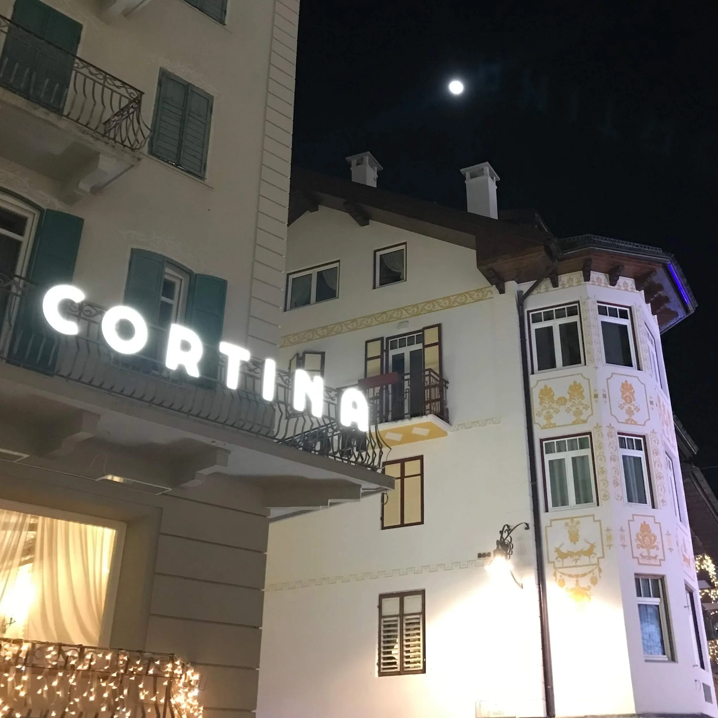 A sign glows with the word CORTINA in Cortina d'Ampezzo at night.