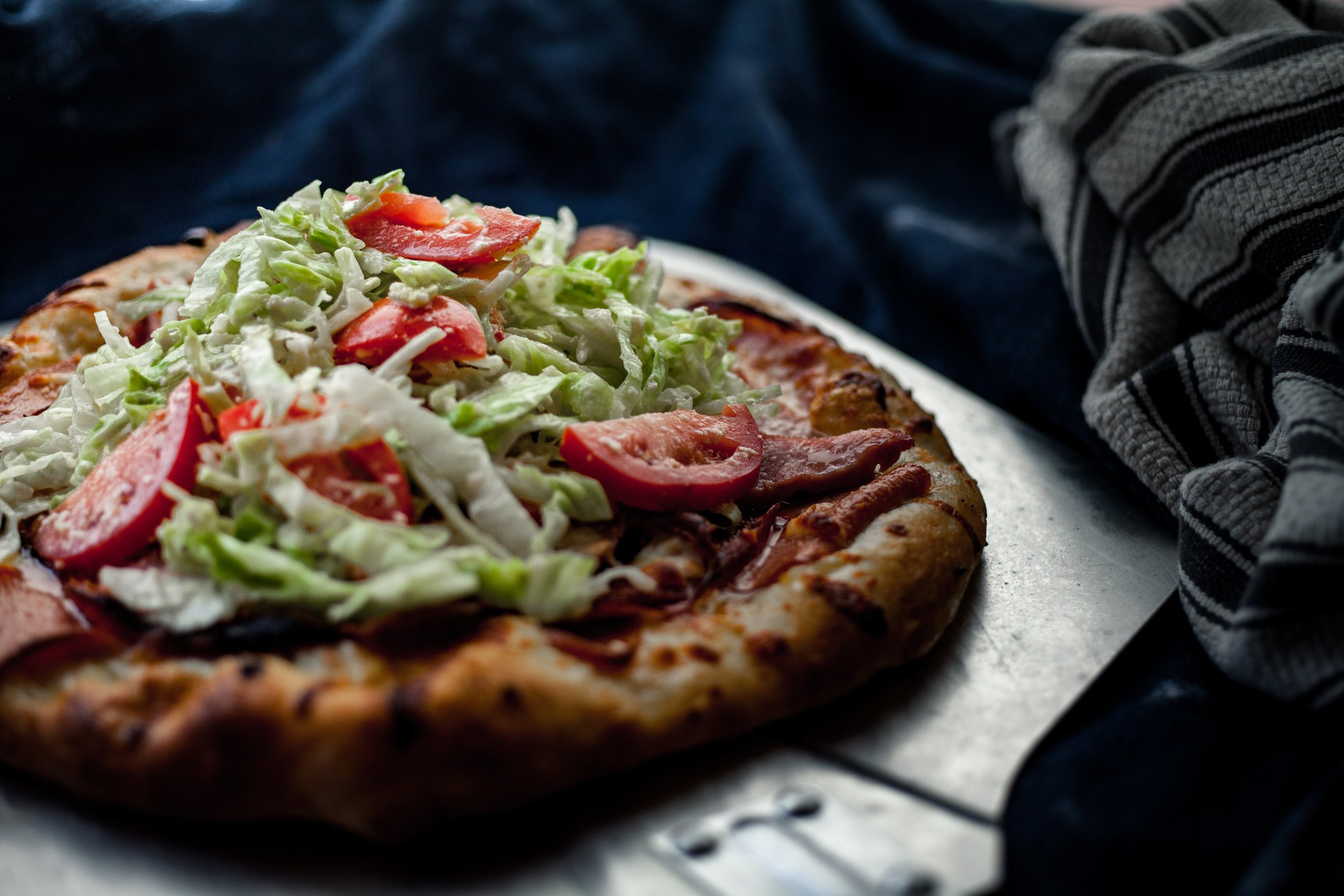 Close-up of a freshly baked pizza with lettuce, sliced tomatoes, and meat toppings on a metal tray.