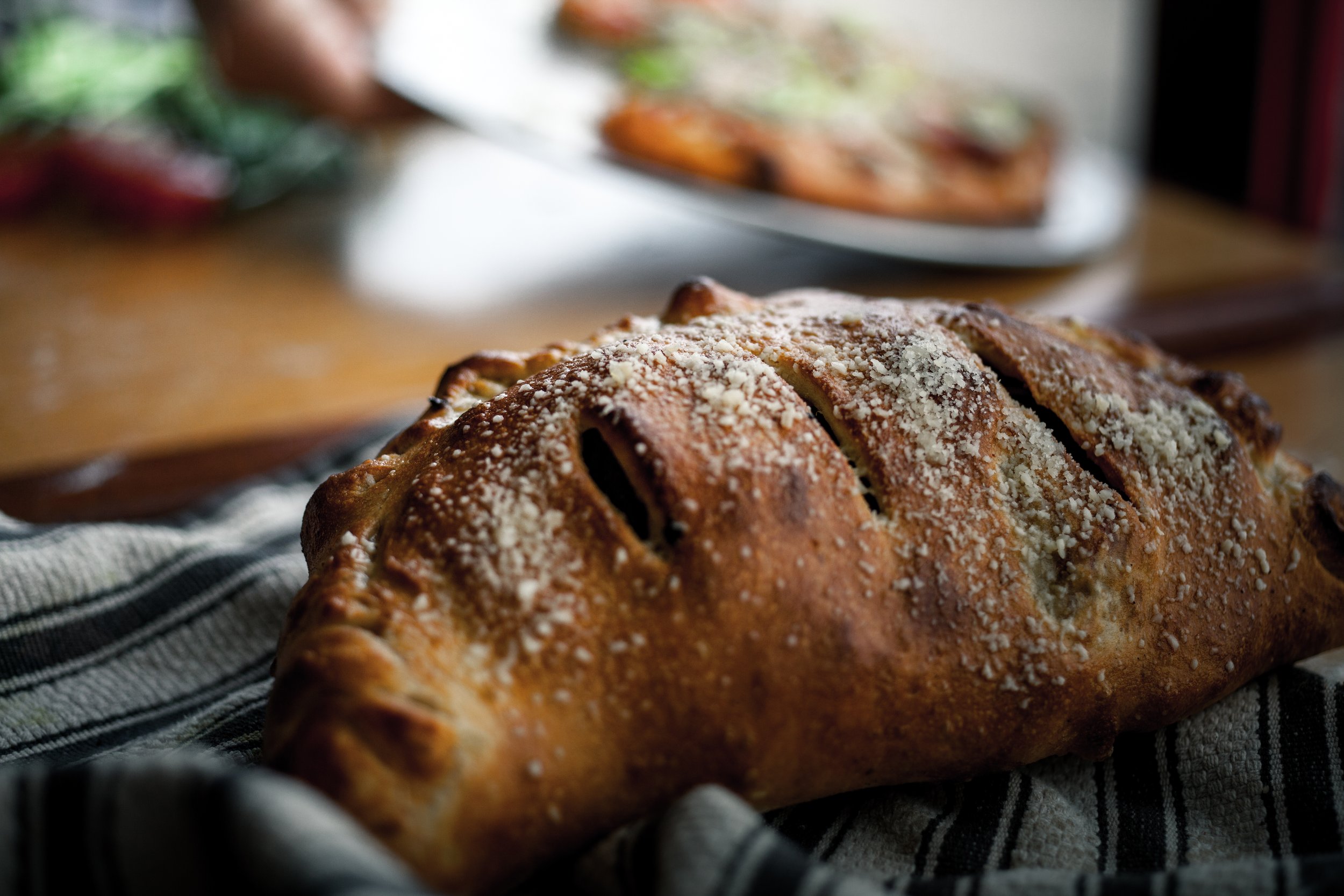Baked pastry with a golden-brown crust, sprinkled with parmesan cheese, resting on a black and white striped cloth.