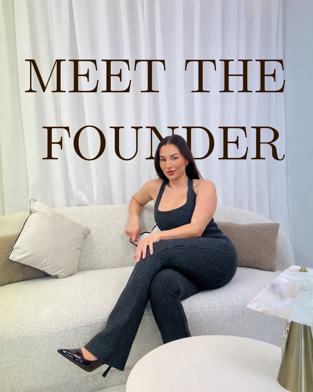 Corrie the founder of The Atelier Society sitting on a light-colored sofa with a cream and a beige pillow, in front of white curtains, with large text saying 'Meet the Founder' overlaid on the image.