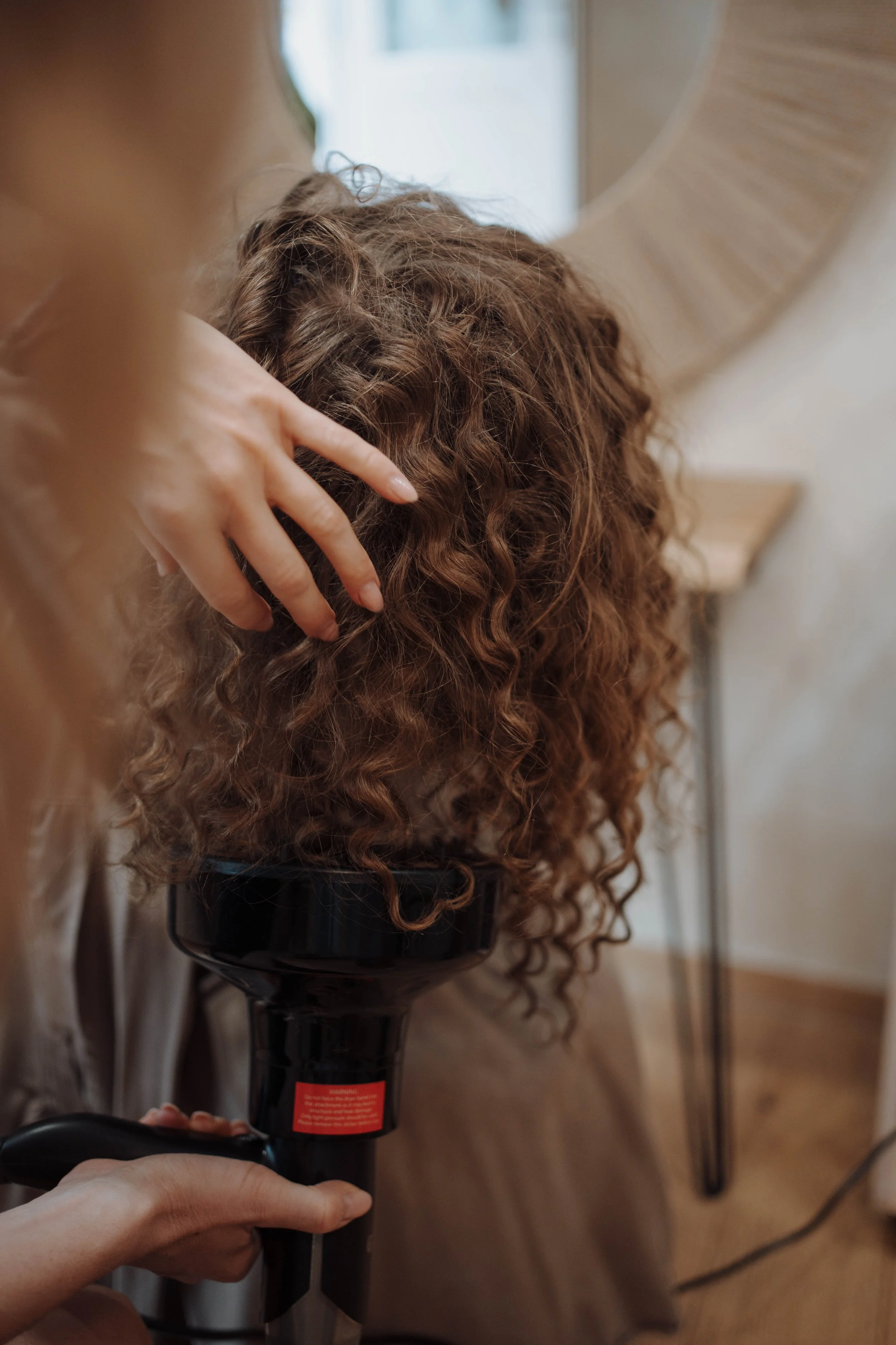 Eine Person trocknet die lockigen Haare einer anderen Person mit einem Haartrockner.