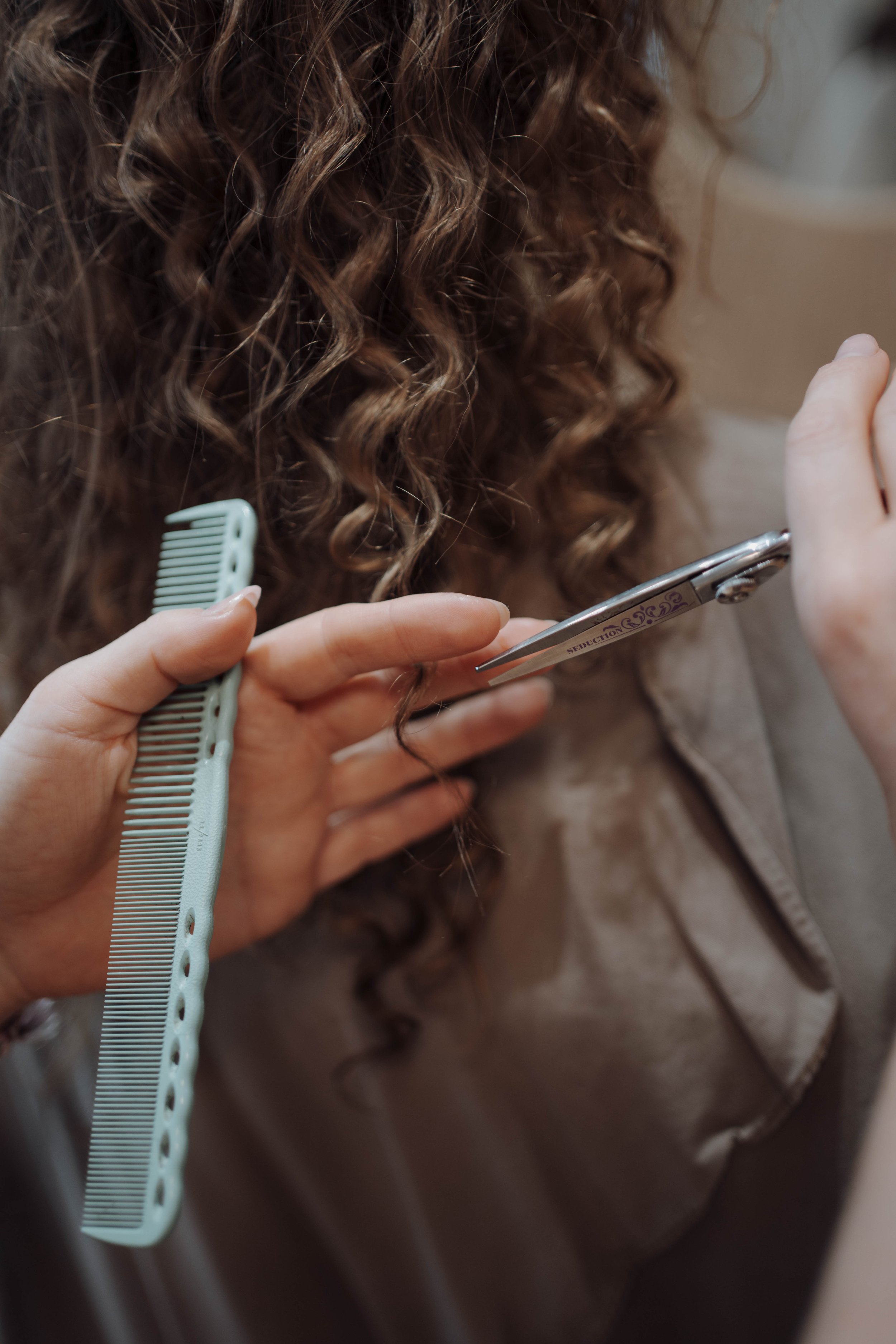 Friseurin schneidet Locken einer Frau mit einer Schere und hält einen Kamm.