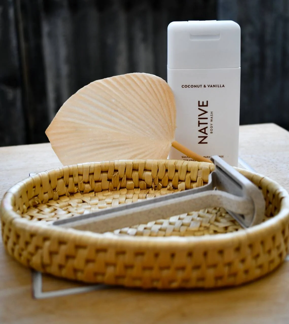 A basket containing a razor with a body wash bottle labeled 'NATIVE' coconut and vanilla behind it, and a background with dark wood paneling.
