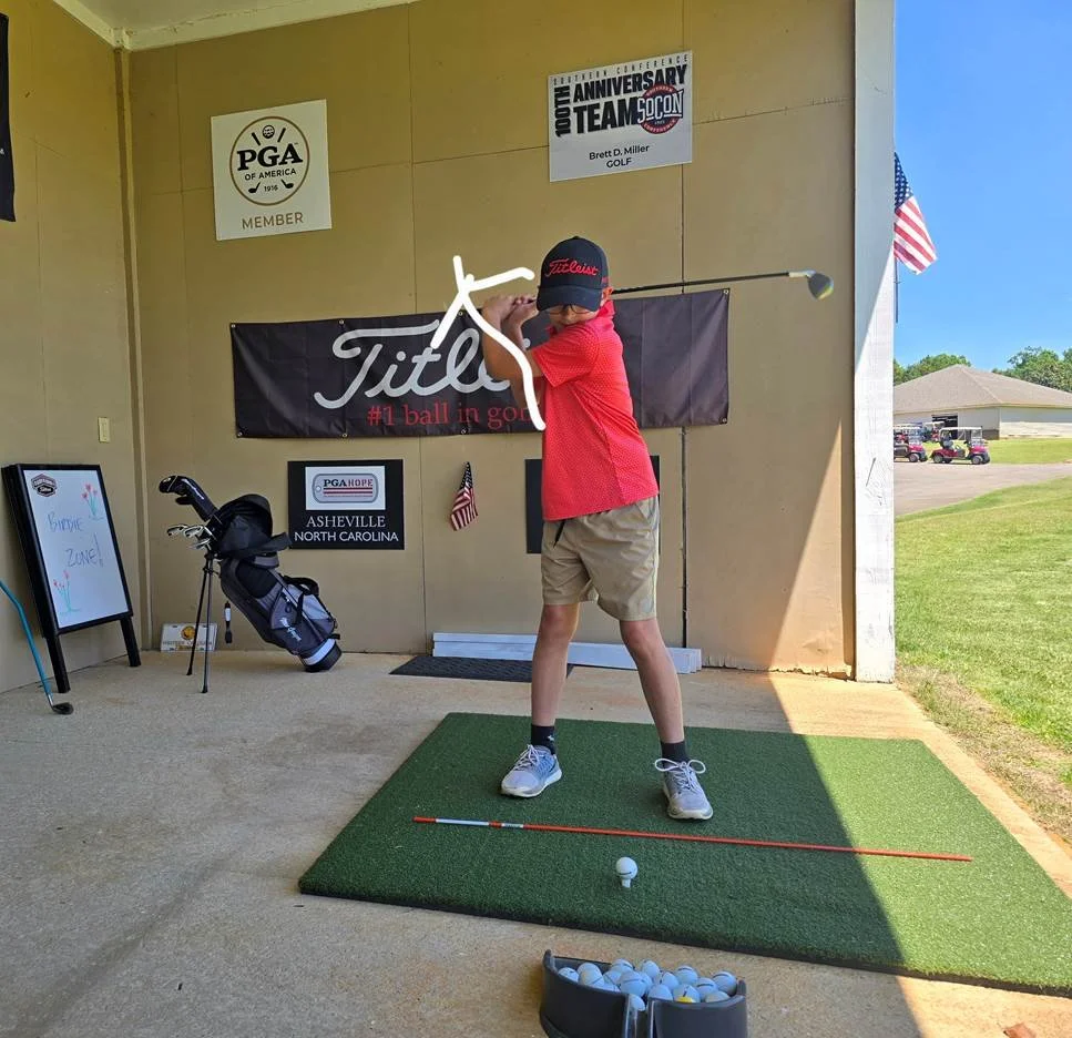 Person in a pink shirt and black shorts swinging a golf club on a golf course.