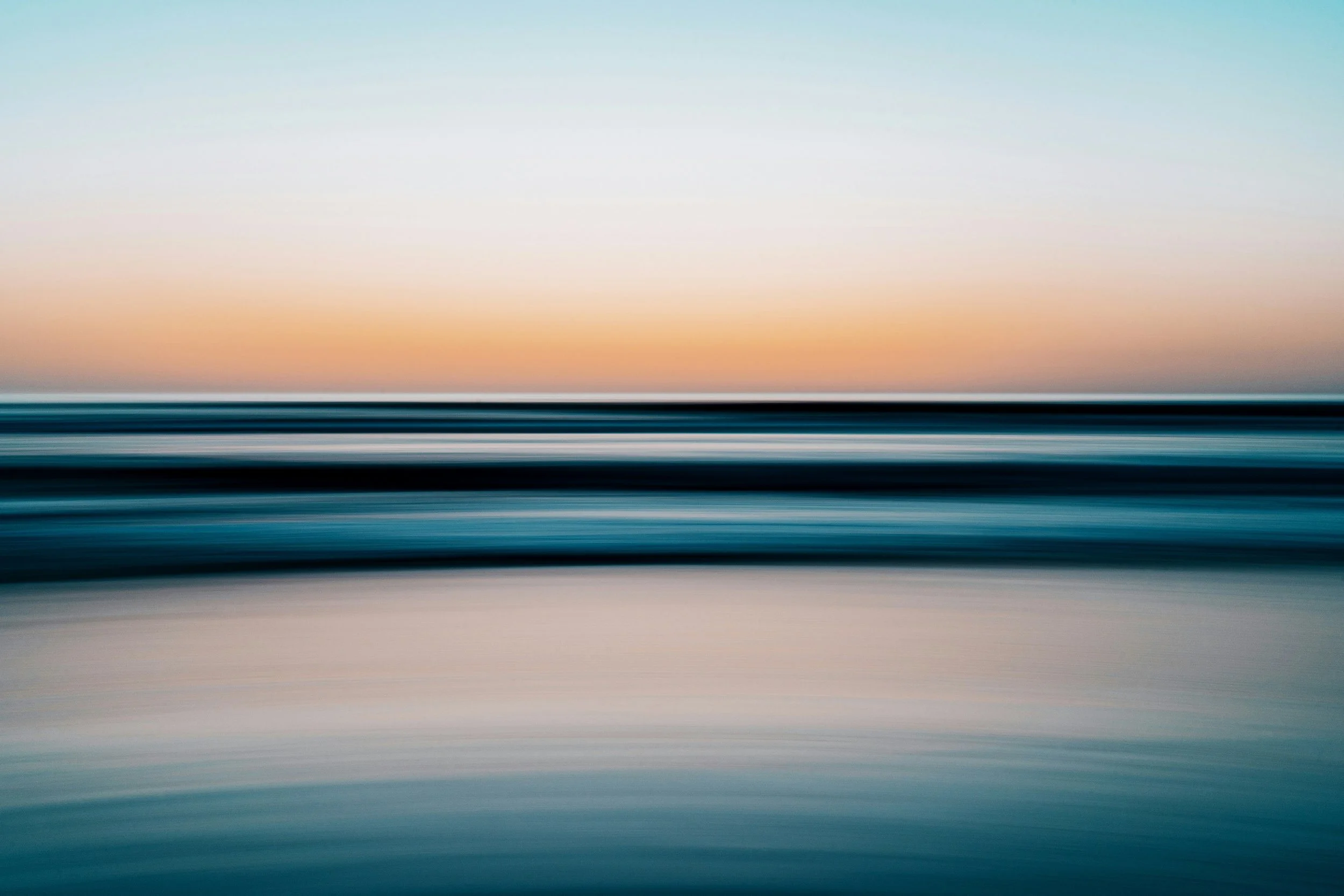 Abstract photo of a calm body of water with horizontal motion blur, with a pastel sky at sunset or sunrise in the background.