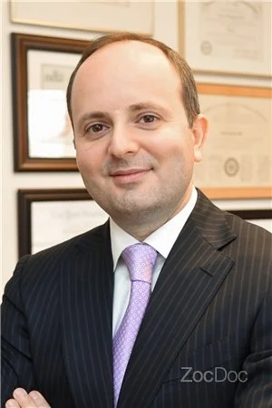 Portrait of a man in a business suit with framed certificates on the wall in the background.