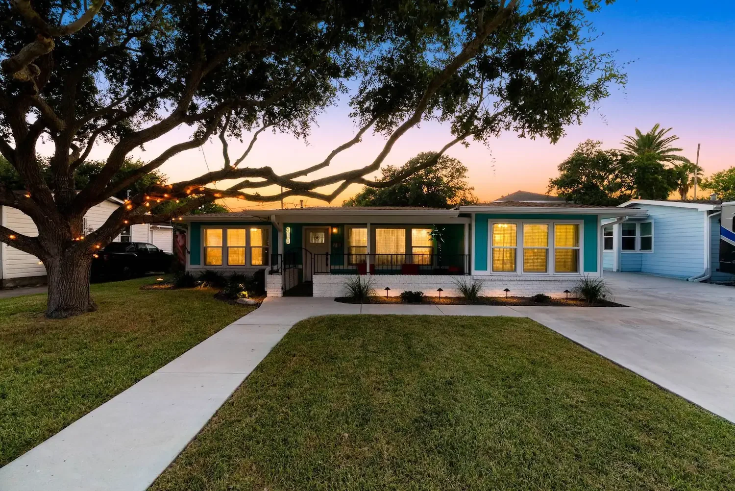 Front exterior of The Oasis at twilight with porch lights on and oak tree