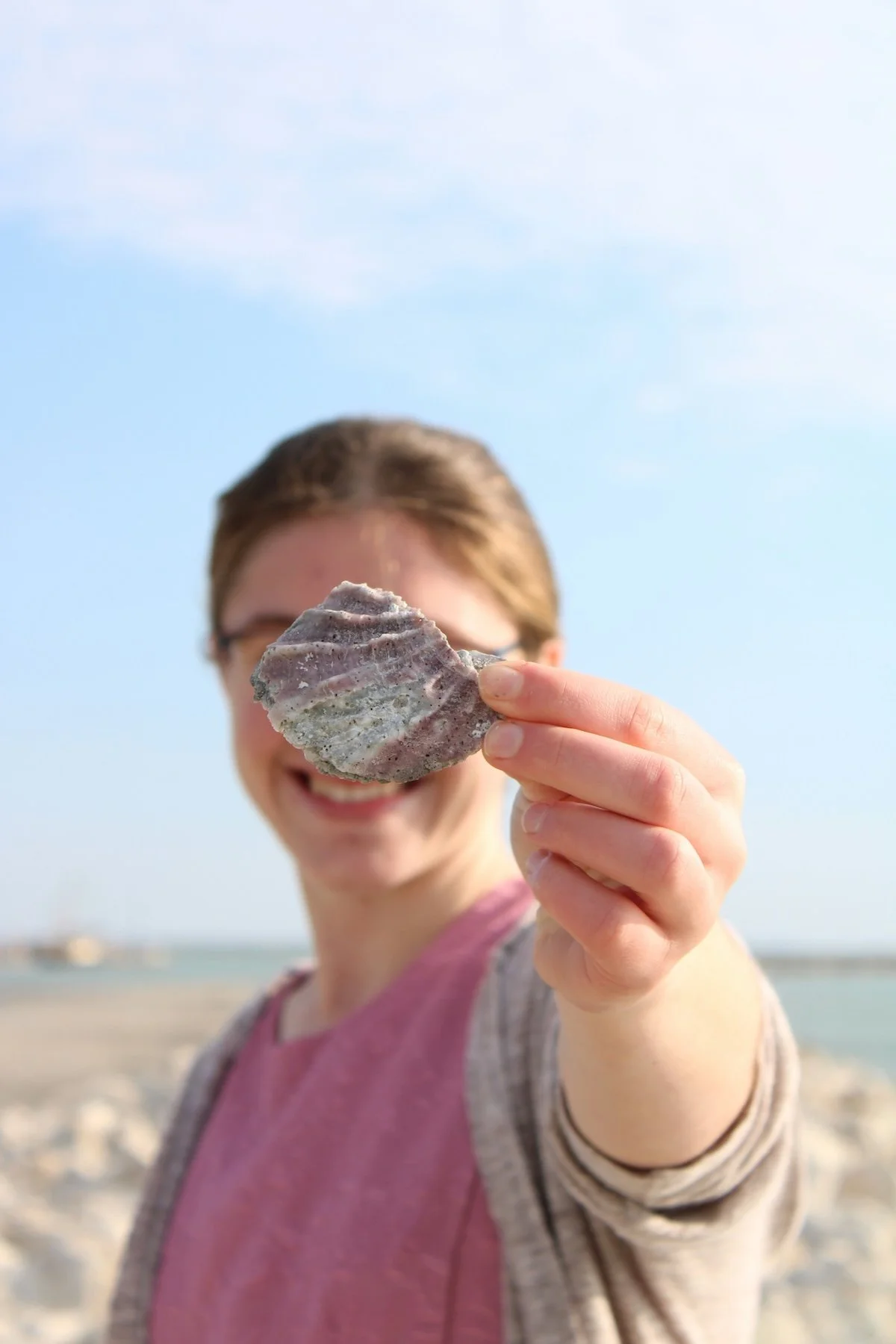 A girl on an Austin beach holding a sea shell.