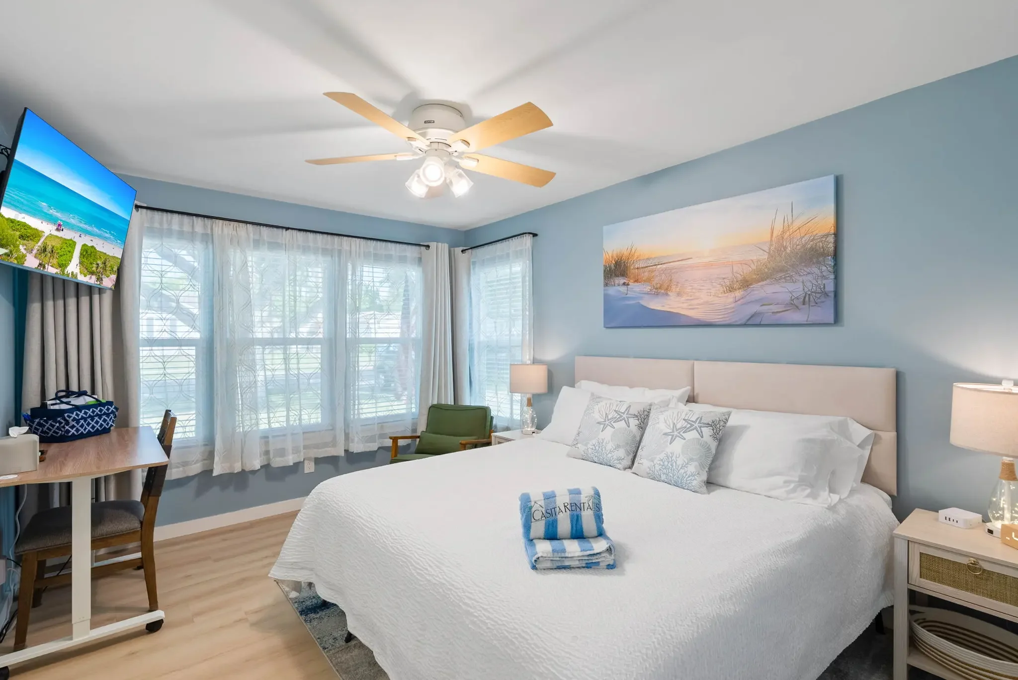 Primary king bedroom with mounted TV and beach art above the headboard