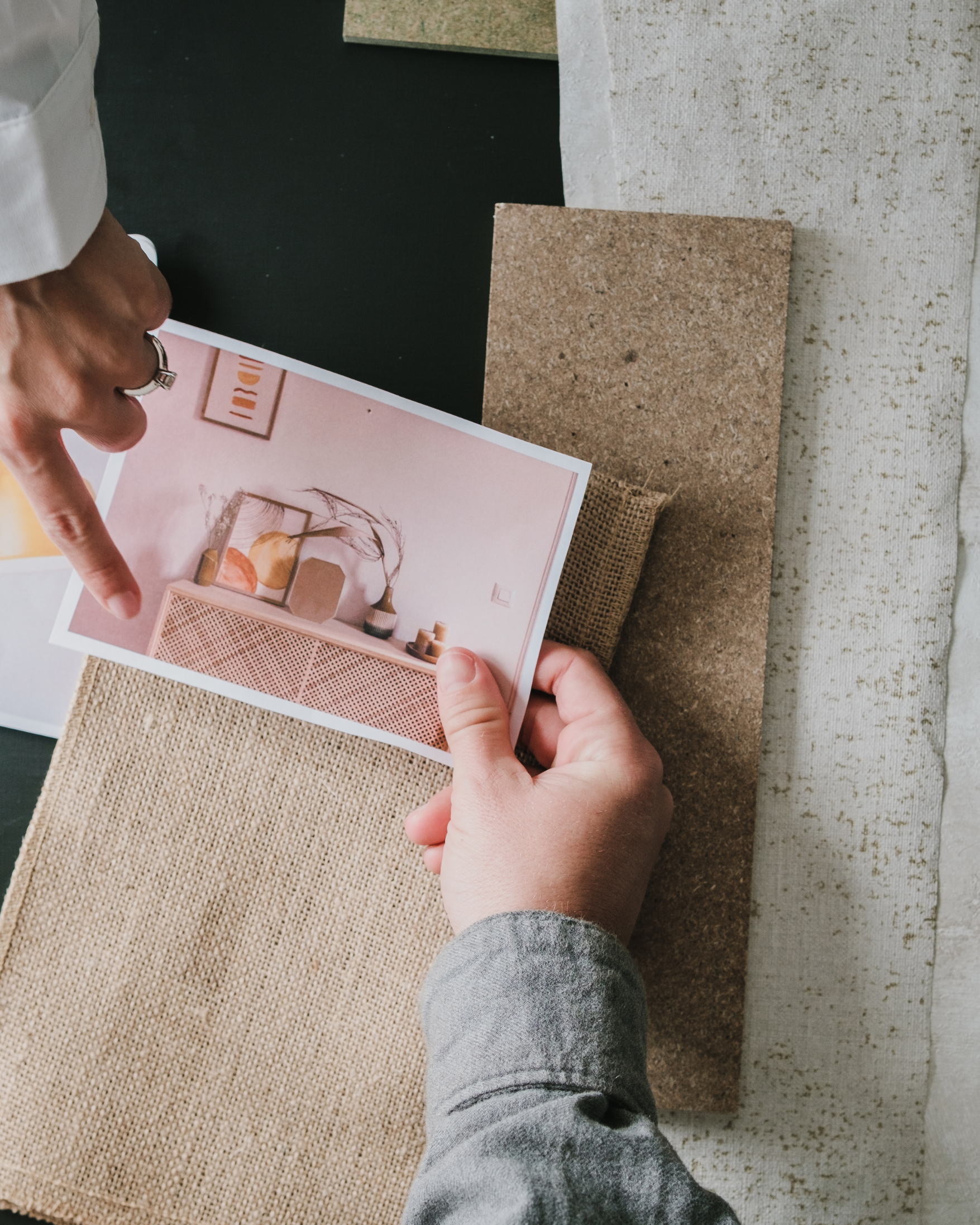 Person, die einen Dekorationsplan betrachtet, mit mehreren Stoffmustern und Keramikdekorationen auf einem Tisch