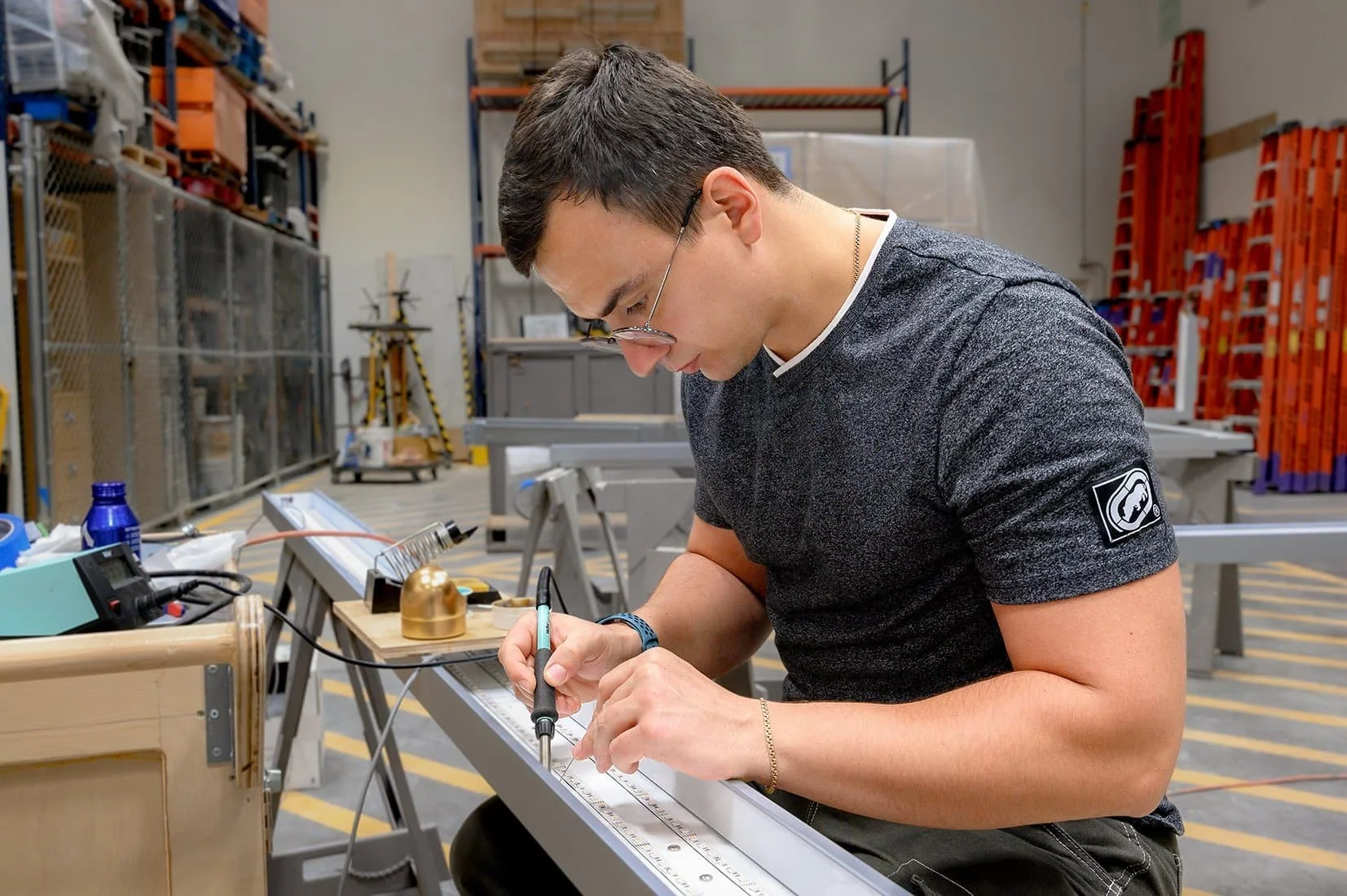 A young man working on a technical project in a workshop, using a laser measuring device on a piece of metal.