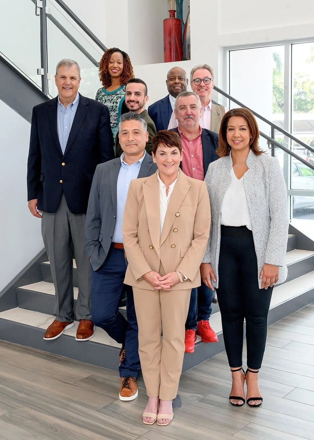 Group of ten diverse professionals posing on a staircase inside a modern office building.