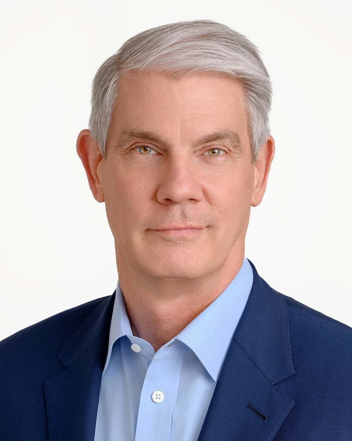 Portrait of a middle-aged man with gray hair, wearing a dark blue suit and light blue shirt, against a plain white background.