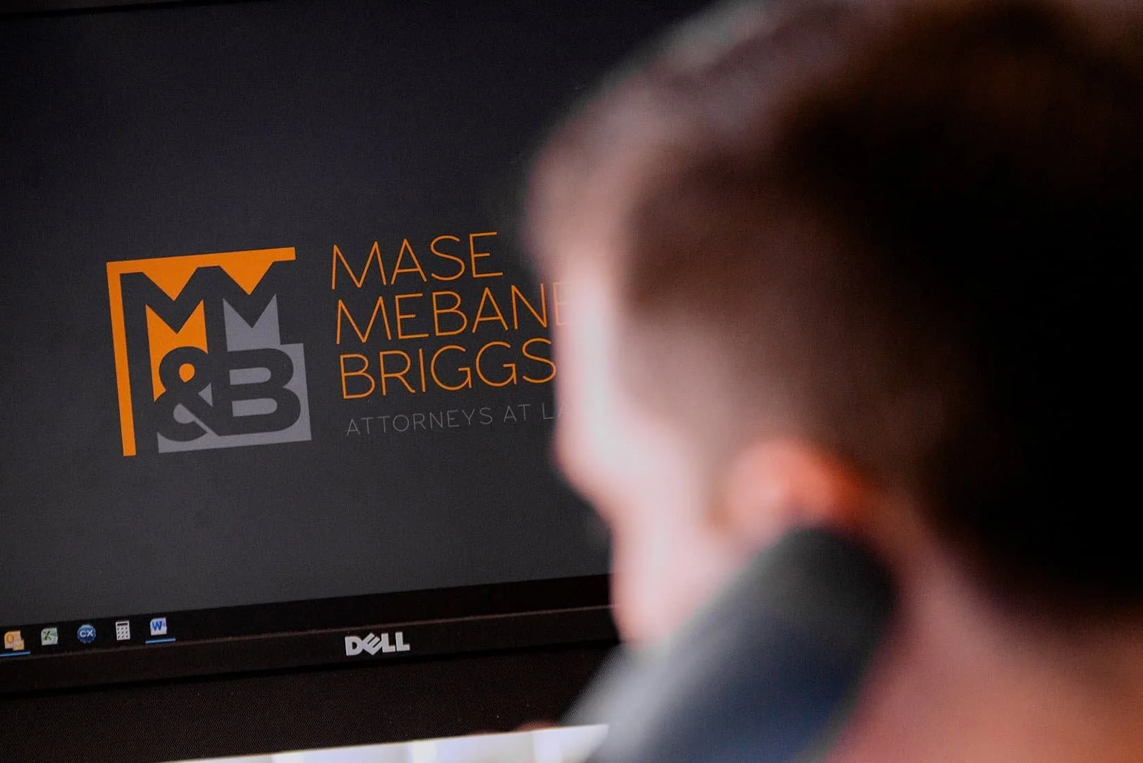 A person with brown hair is looking at a computer screen displaying the logo and name of a law firm, Mase Mebane Briggs, along with the text "Attorneys at L".