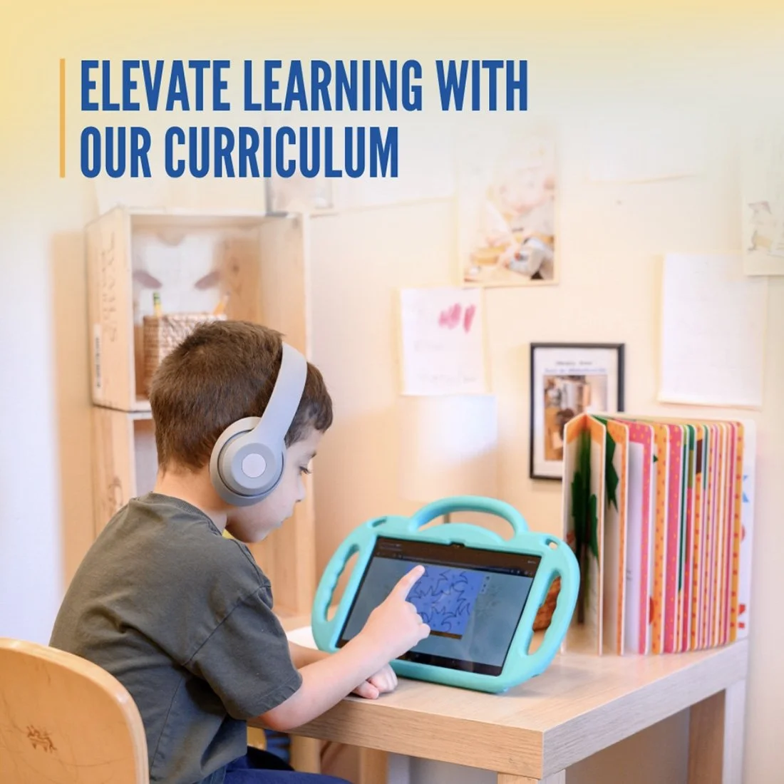 Young boy with headphones using a tablet with a blue case on a wooden desk, in a room decorated with colorful folders and artwork on the wall, with a sign that says 'Elevate Learning with Our Curriculum'.