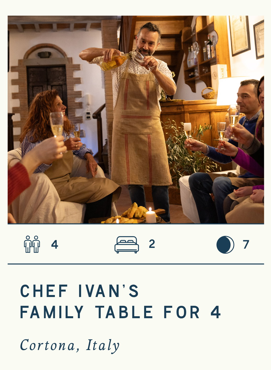 Chef Ivan serving drinks to four guests at a family dinner in Cortona, Italy, with warm lighting, cozy indoor decor, and a plate of food on the table.