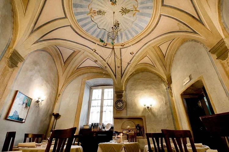 Interior of a historic restaurant with arched ceilings, decorative frescoes, a large window, and tables set for dining.