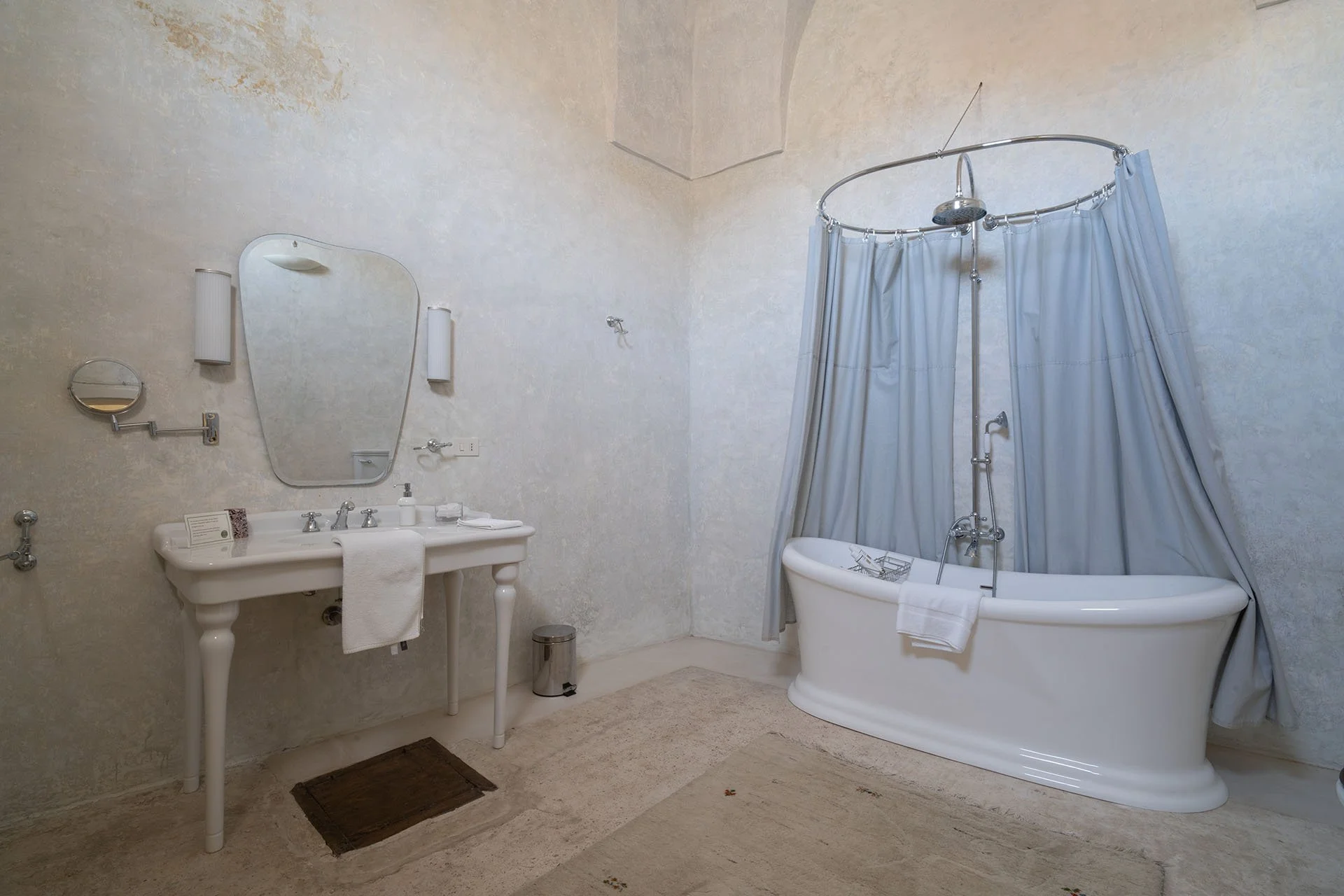 A vintage-style bathroom with a white freestanding bathtub with curtains, a white sink with accessories, and a large mirror.