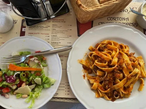 A plate of pasta with sauce and a side salad with lettuce, cherry tomatoes, and carrots on a table at a restaurant.