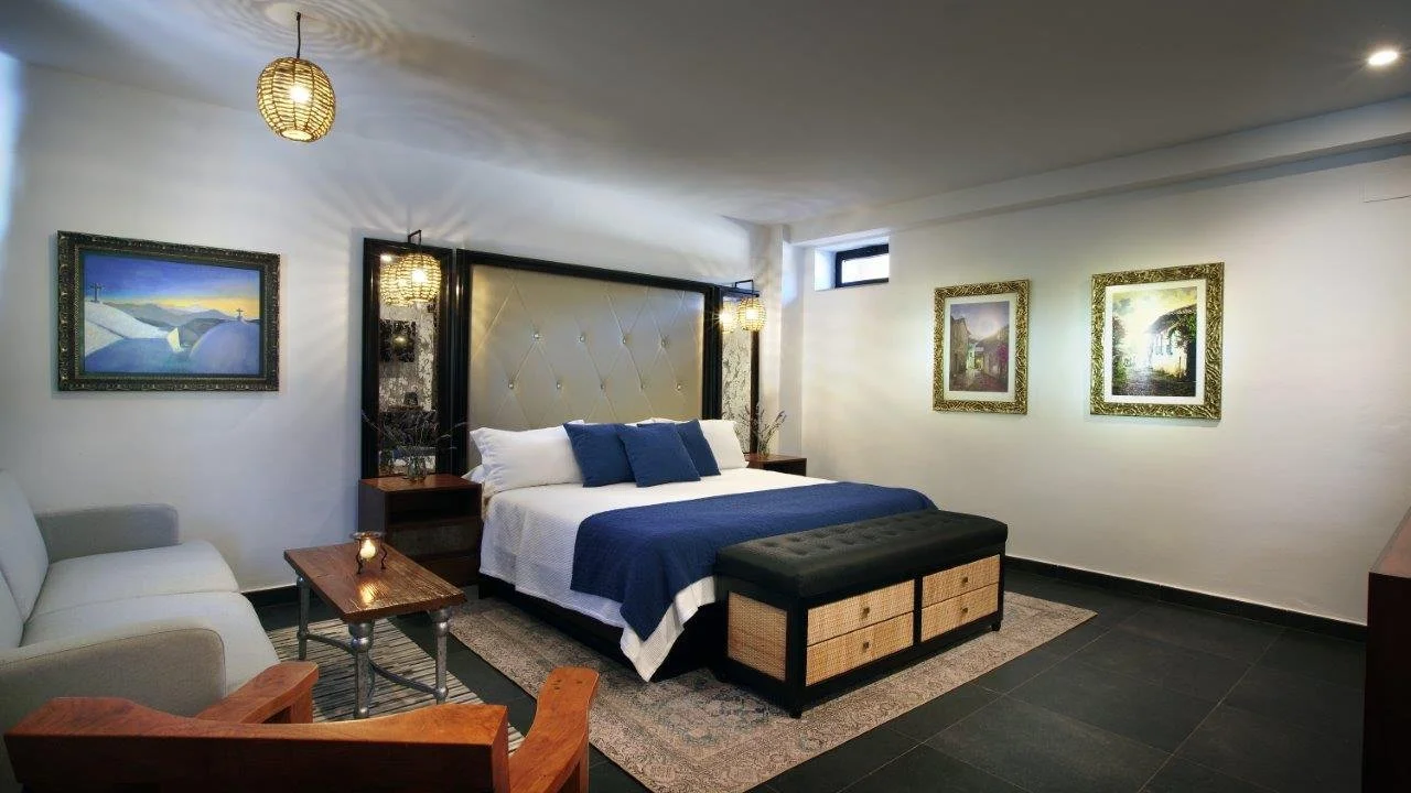 A modern bedroom with a large bed, blue accents, and artwork on white walls, decorated with hanging lamps.