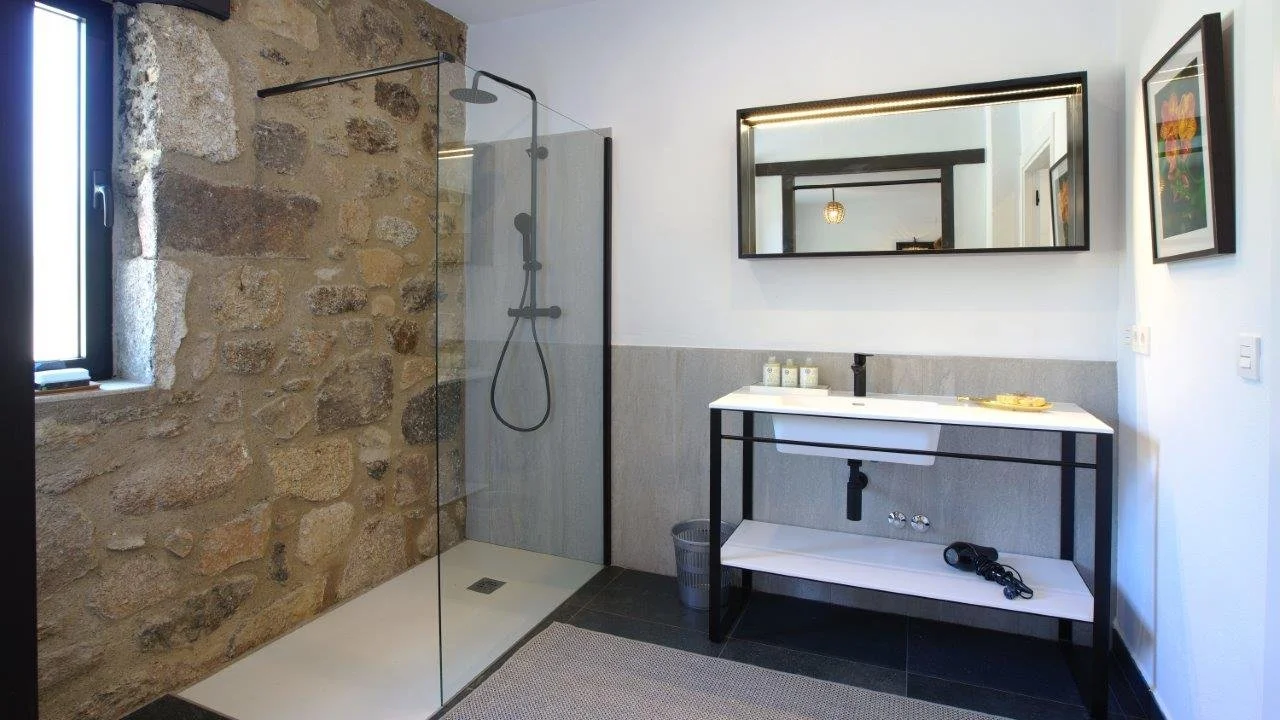 Modern bathroom with a stone wall shower area, black framing, a large mirror, and a white vanity with black fixtures.