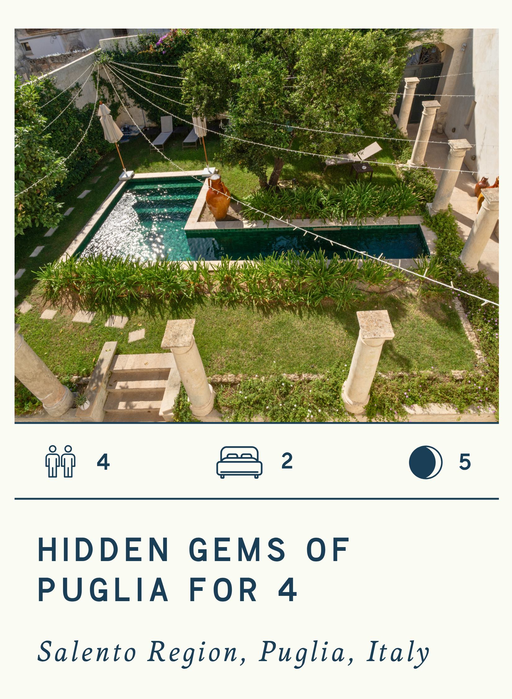 An aerial view of a Mediterranean-style garden with a small rectangular swimming pool, surrounded by lush green plants, trees, and stone columns. String lights are hung above the garden, and there are lounge chairs on the grass.