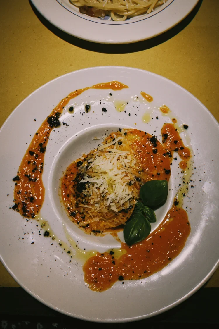 A plate of spaghetti with tomato sauce, topped with shredded cheese and garnished with fresh basil leaves, with additional sauce and black pepper around the dish.