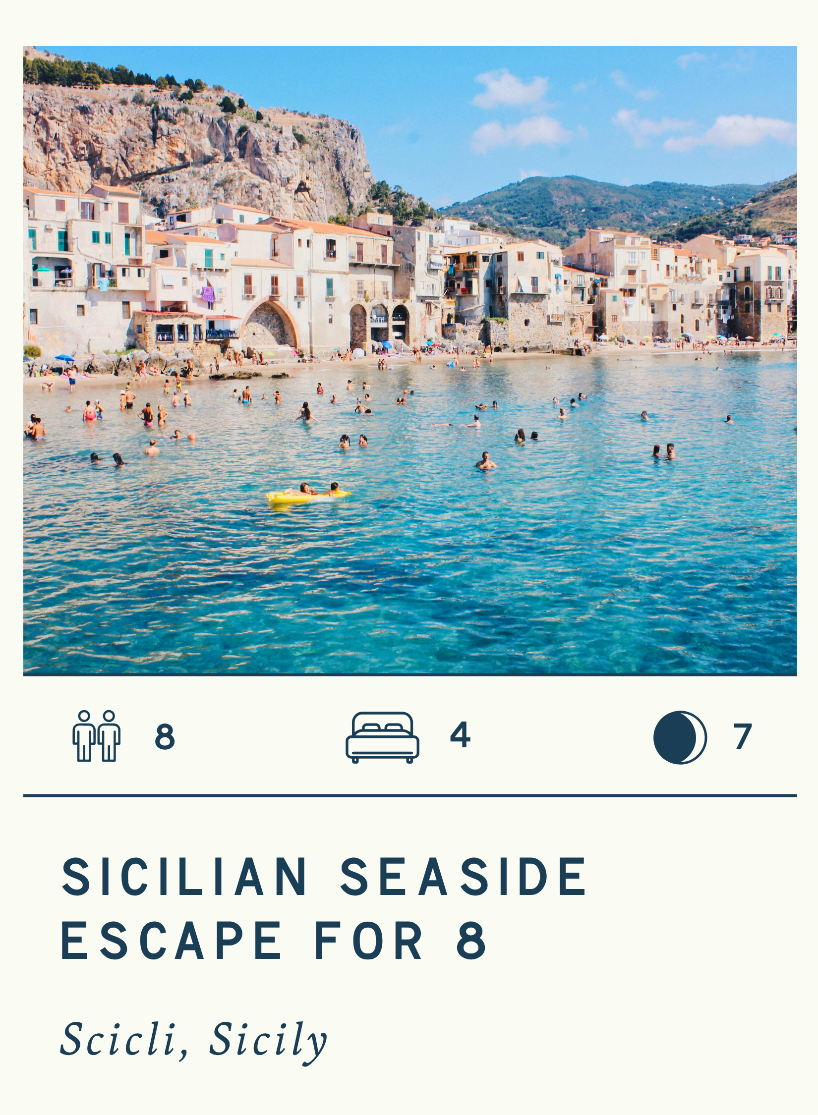 A colorful seaside village with buildings along the water's edge, people swimming and relaxing in the sea, hills in the background, and clear blue sky.