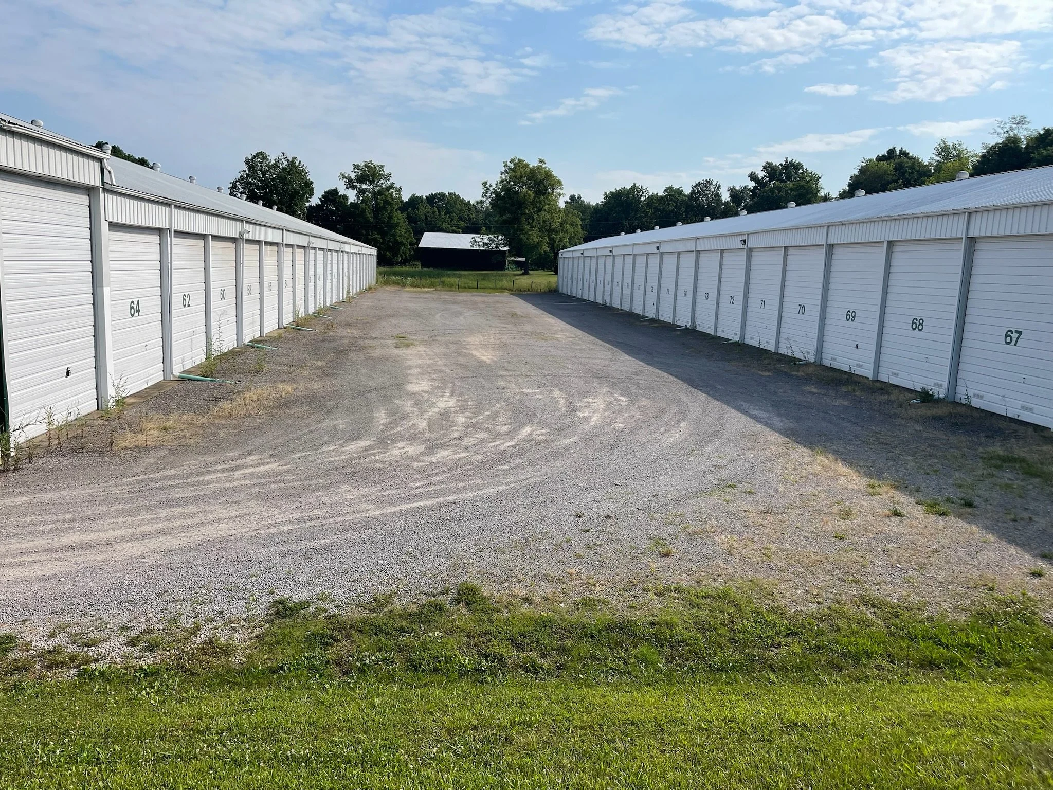 Row of white storage units with numbered doors, and a gravel parking area.
