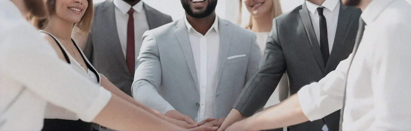A diverse group of professionals in business attire, standing in a circle with their hands stacked together in the center, symbolizing teamwork and unity.
