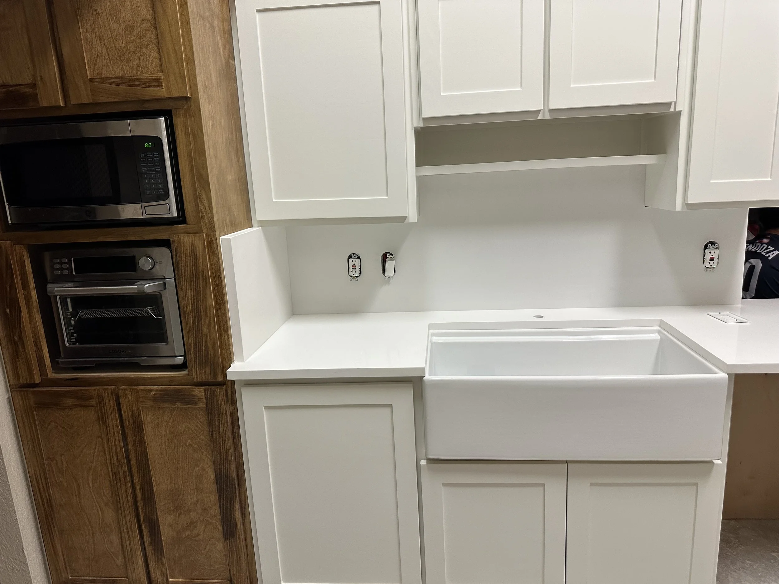 Kitchen with white cabinetry, a large white utility sink, a microwave, and an oven in a space under renovation.