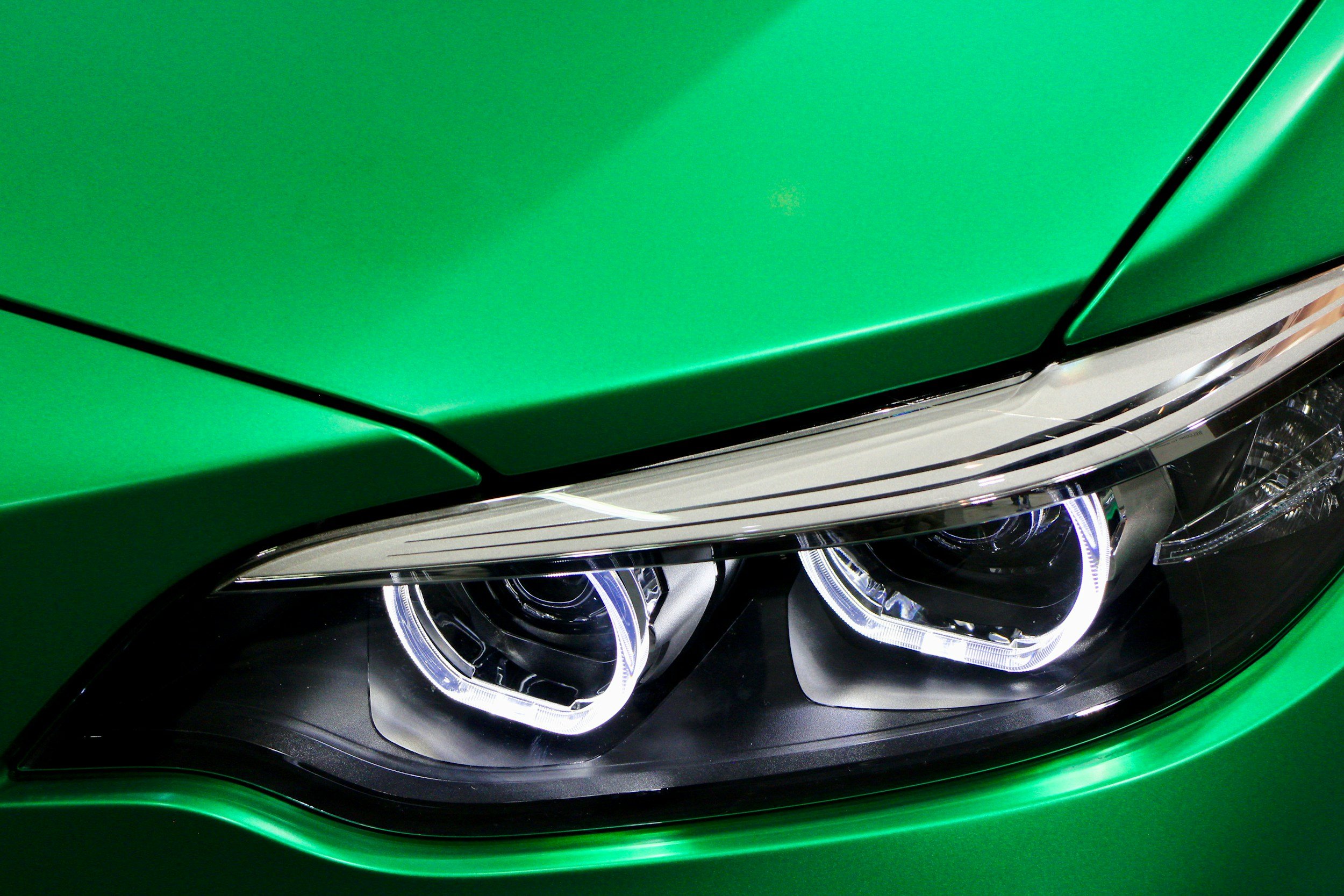 Close-up of a green car’s front with illuminated headlights.