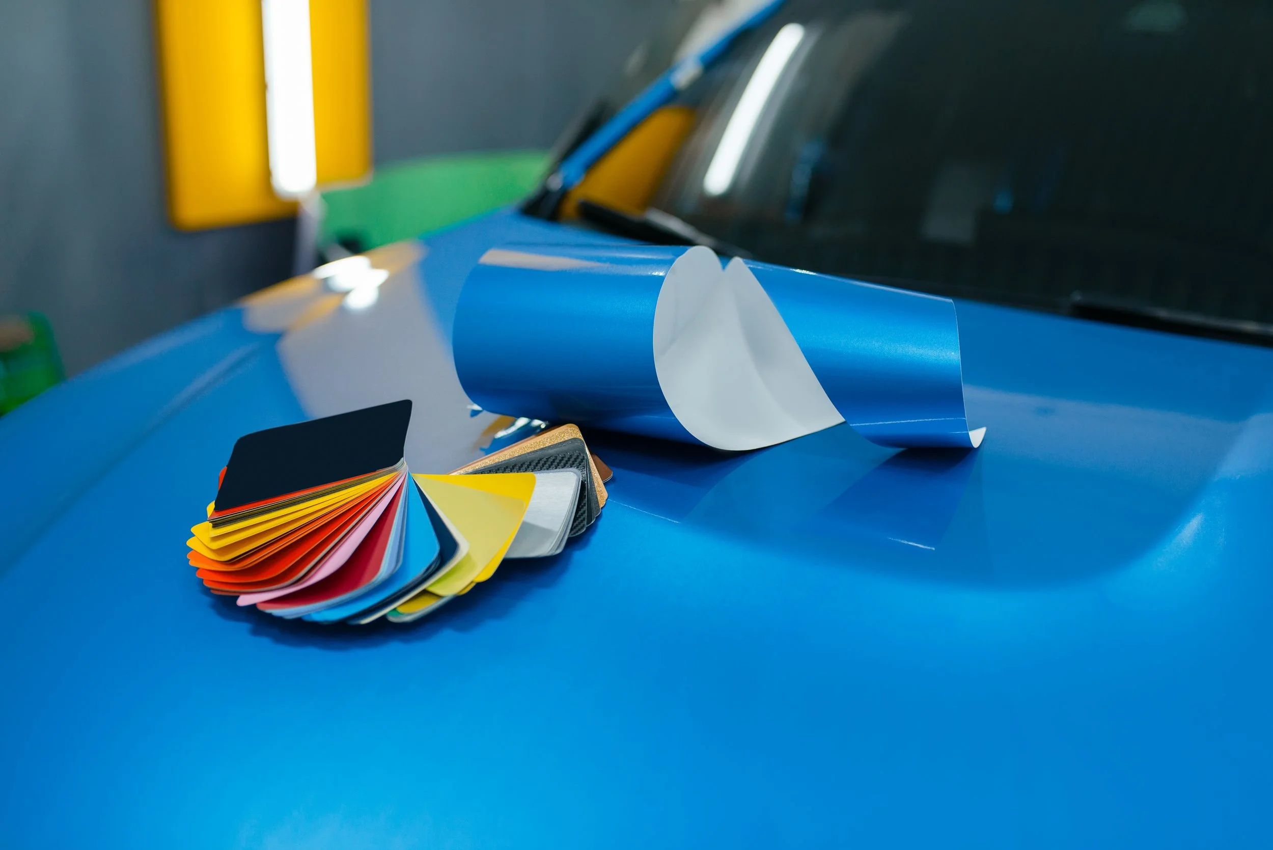 Color swatches, a color sample book, and color film sheets arranged on a blue car hood during a color matching process.