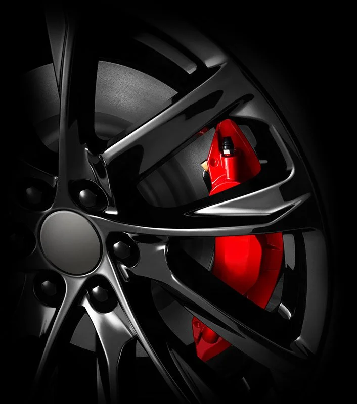 Close-up of a black car wheel with a red brake caliper visible behind it.