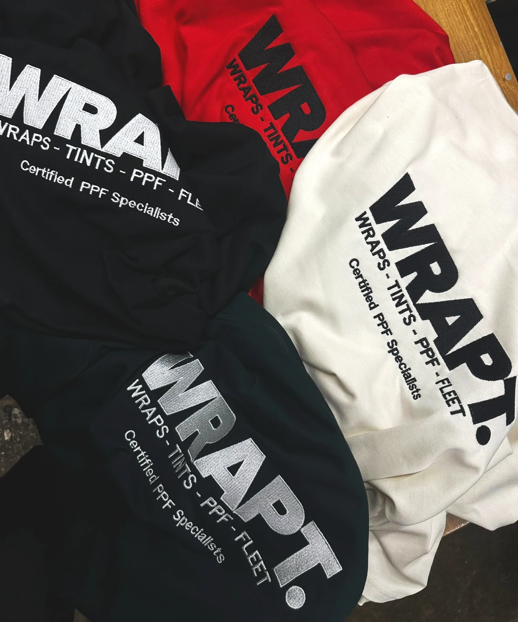 Three shirts with the logo and text for WRAFT, wrapped TIGHTS, PPF, FLEET, and certified PPF specialists in black, red, and white colors.