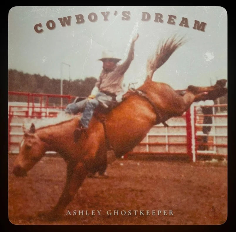 A person riding a bucking horse in a rodeo arena with the text 'Cowboy's Dream' at the top and 'Ashley Ghostkeeper' at the bottom.