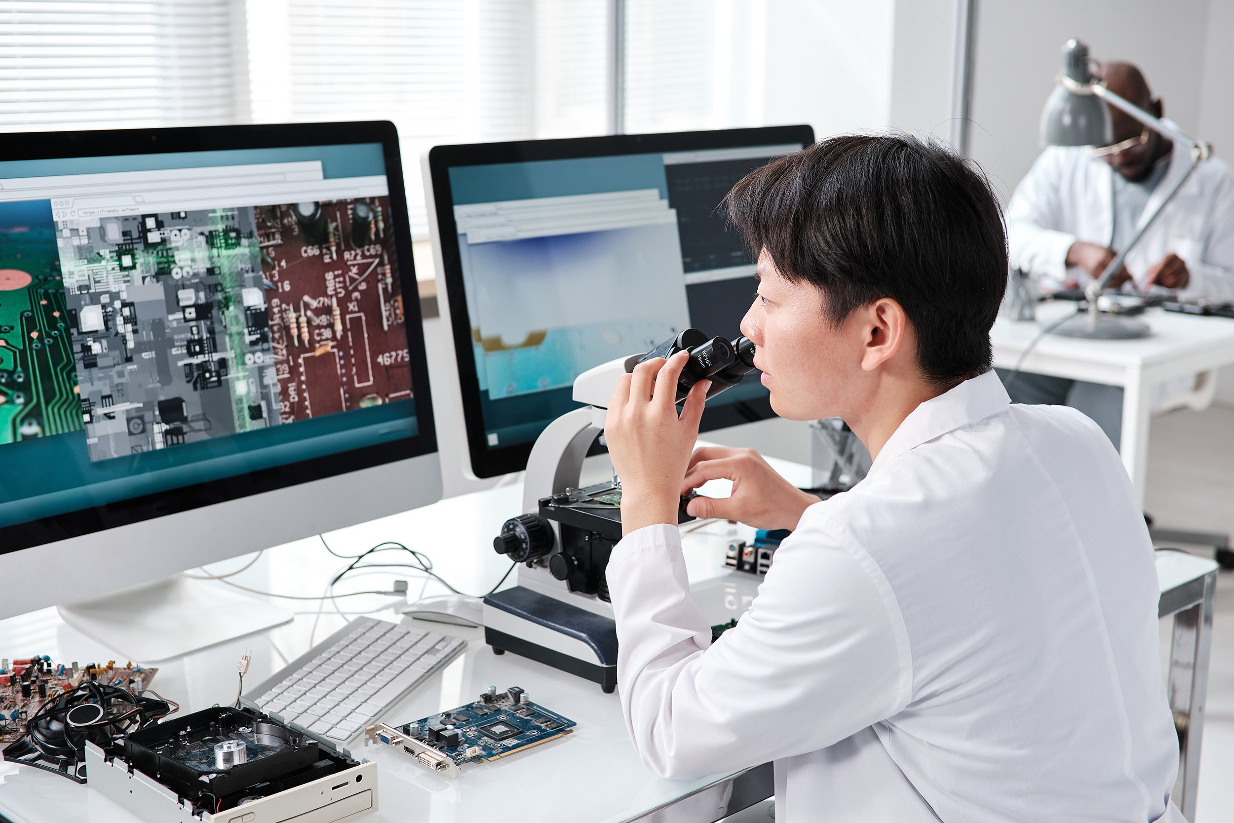 Electronics technician examining circuitry with a microscope