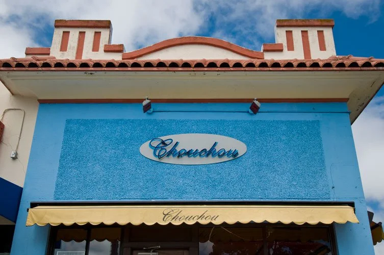 Exterior of a building with a blue facade, a yellow awning, and a sign that reads 'Chouchou' in cursive letters.