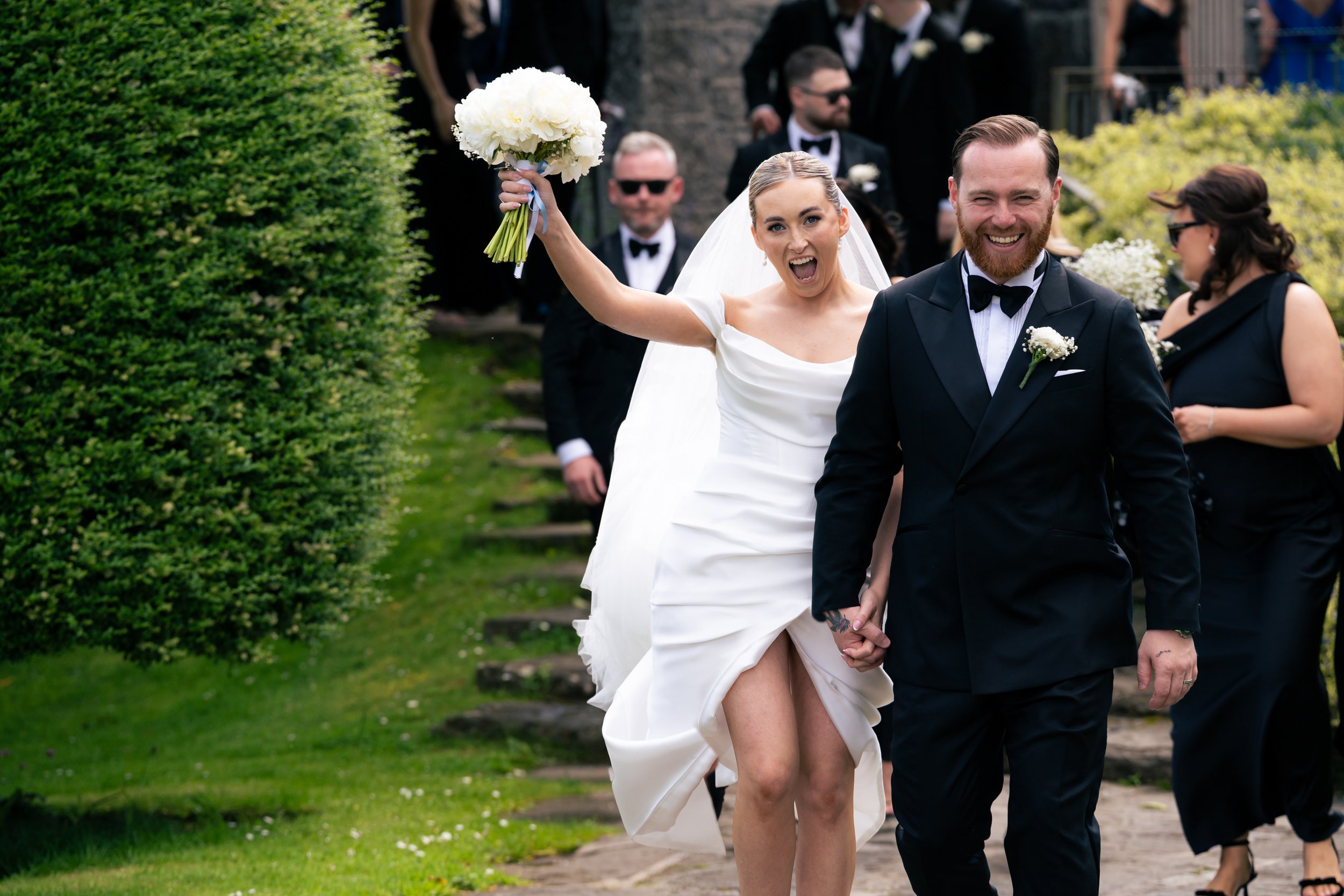 A bride and groom celebrating their wedding with wedding party guests walking outdoors at Ballymagarvey wedding venue, Co. Meath Ireland.