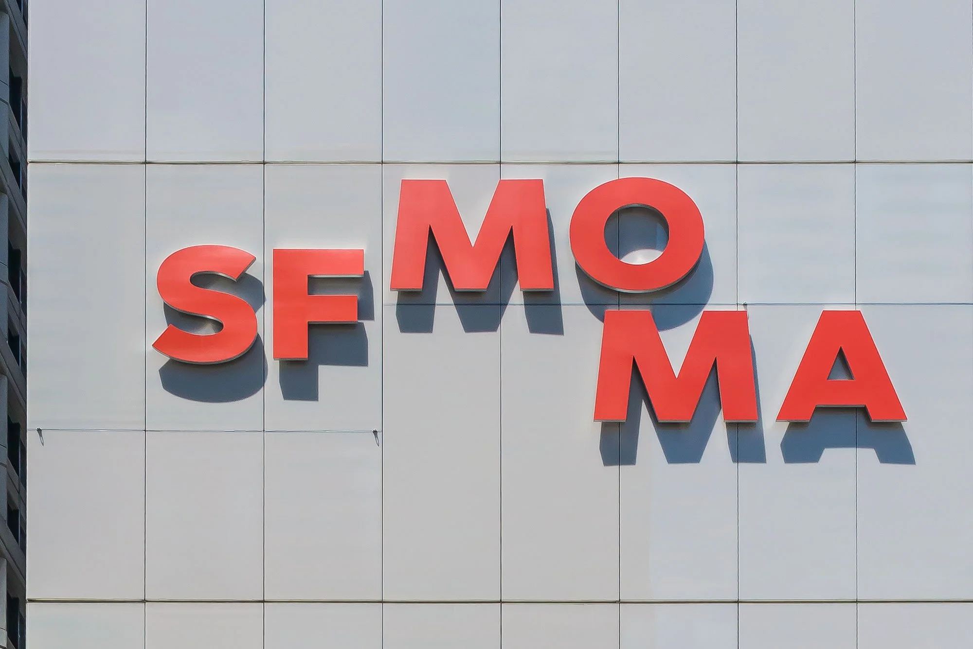 The roof of a building with large red 3D letters spelling out 'SF MOMA' on a white panel background.
