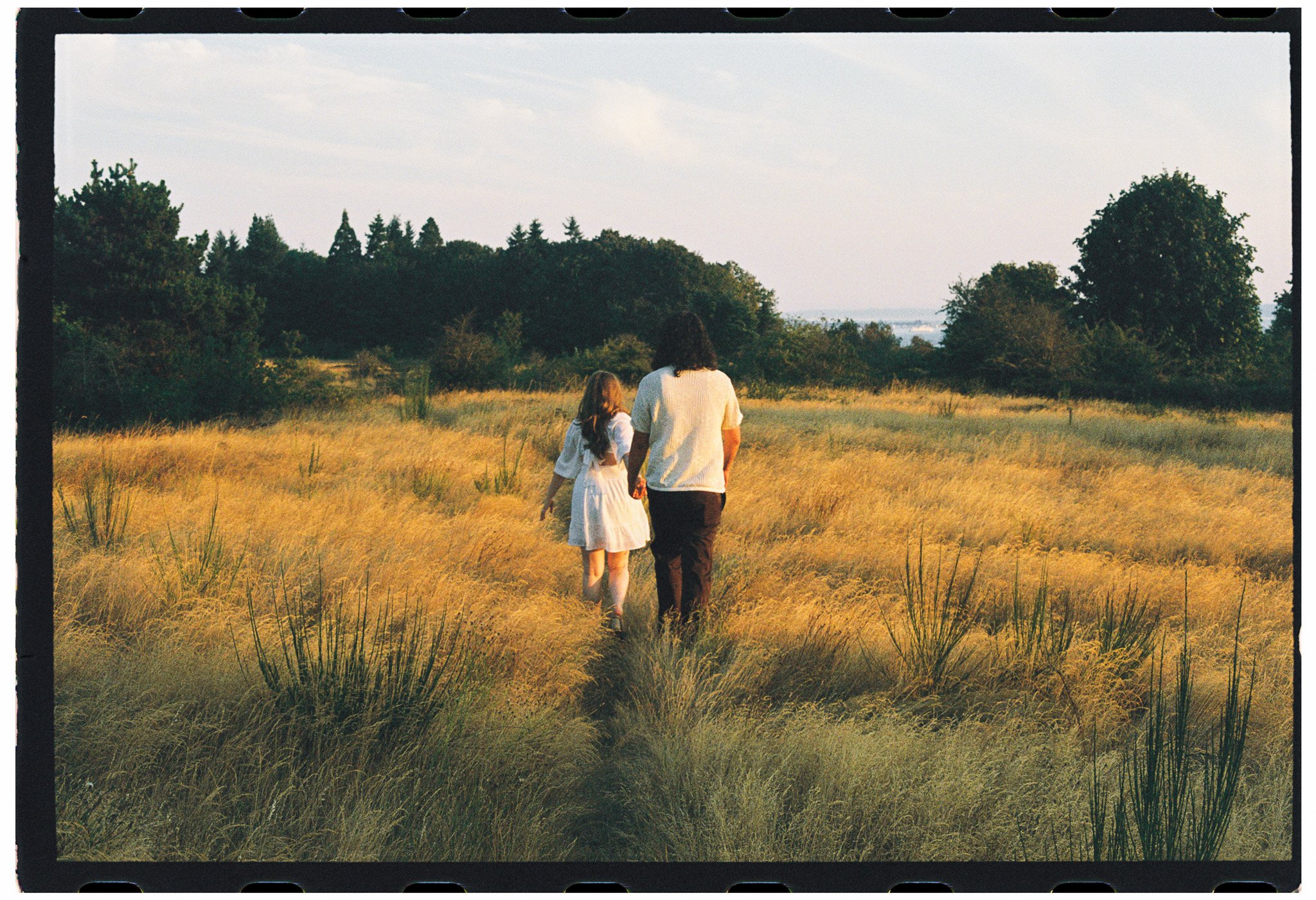 A woman and a girl walking hand in hand through a field for an engagement shoot at Discovery Park in Seattle, Washington