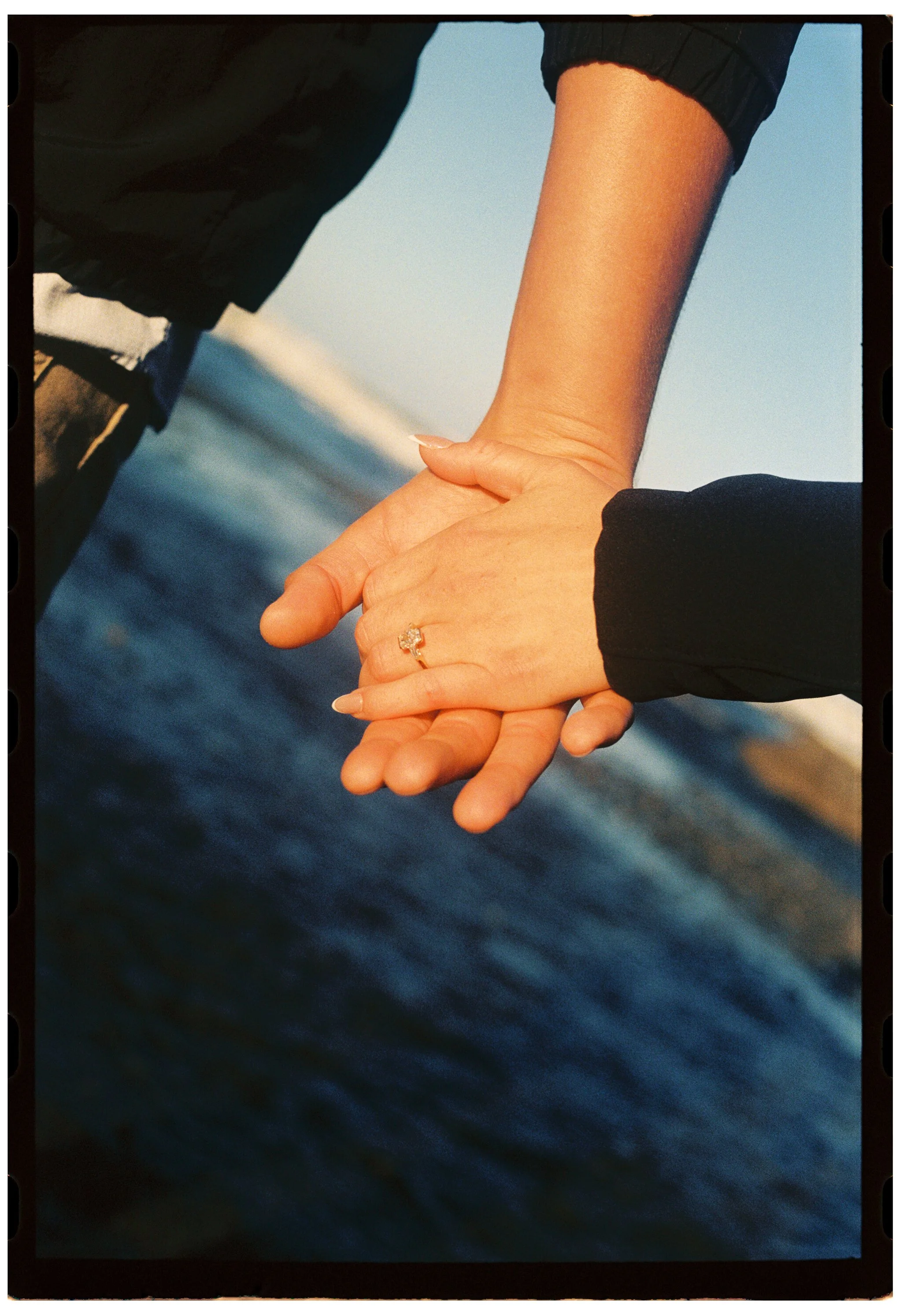 engagement portrait of two hands holding each other over a body of water on Ruby Beach, Olympic Peninsula
