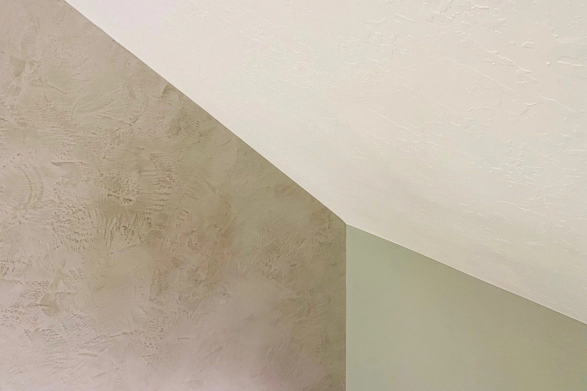 Close-up image of the ceiling corner showing texture and paint color differences between two walls and ceiling.