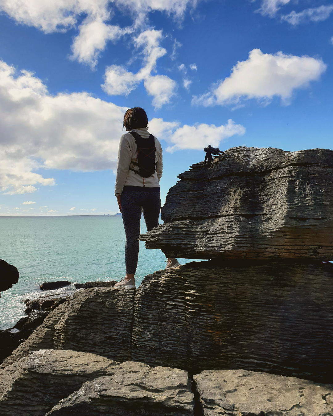 Woman standing on a rock looking out over the sea, symbolising a highly sensitive woman stepping beyond scarcity into spacious possibility.