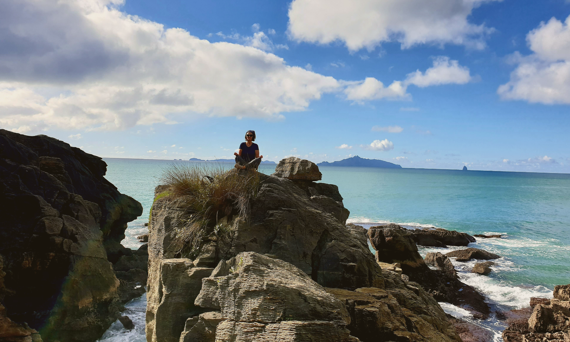 Jocelyn sitting on coastal rocks overlooking the ocean — nature-led reflection and grounding for highly sensitive, high sensation seeking women