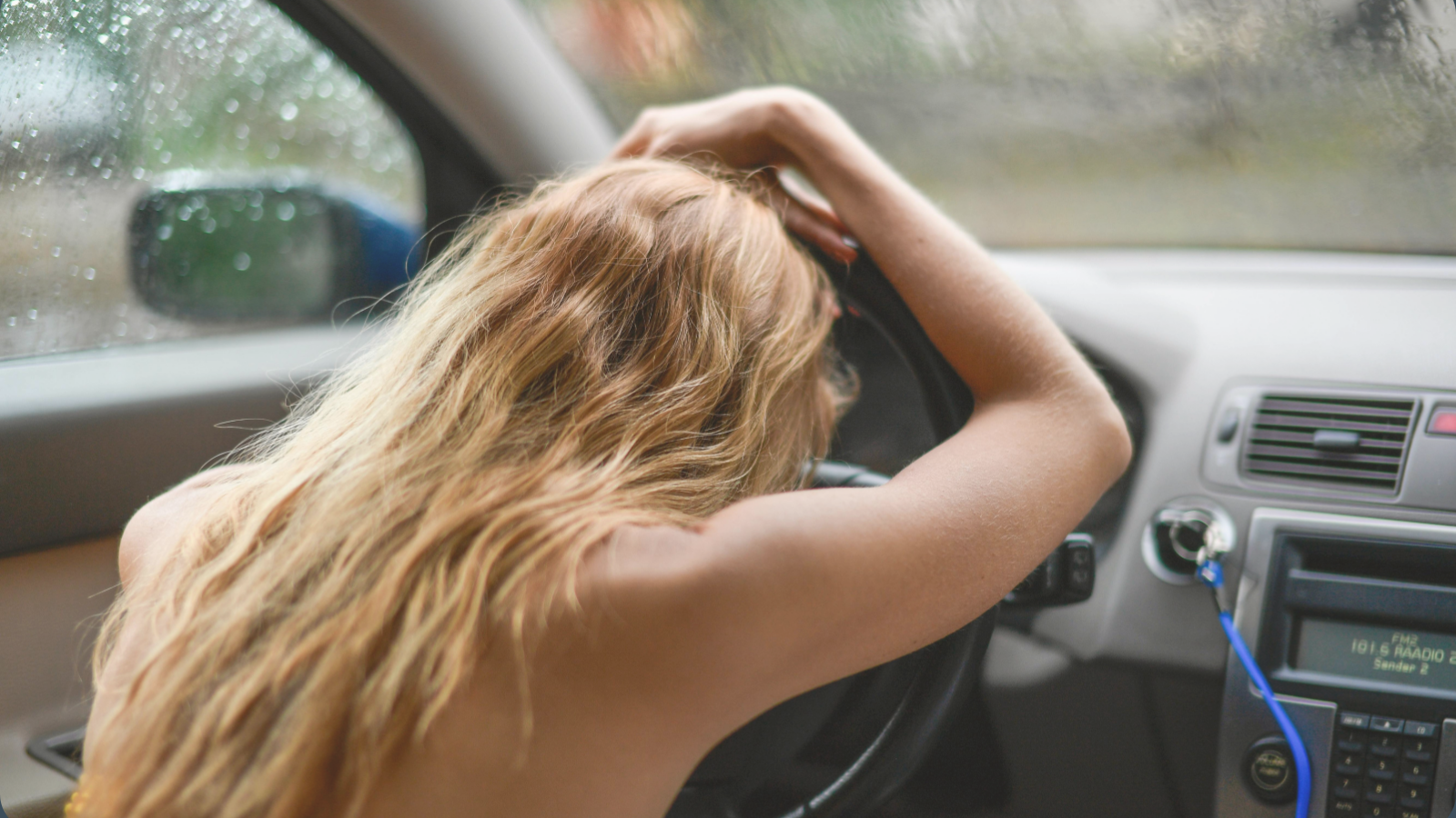 Woman sitting overwhelmed in a parked car during rain, illustrating nervous system overload, emotional exhaustion, and sensory overwhelm in dual-wired women.