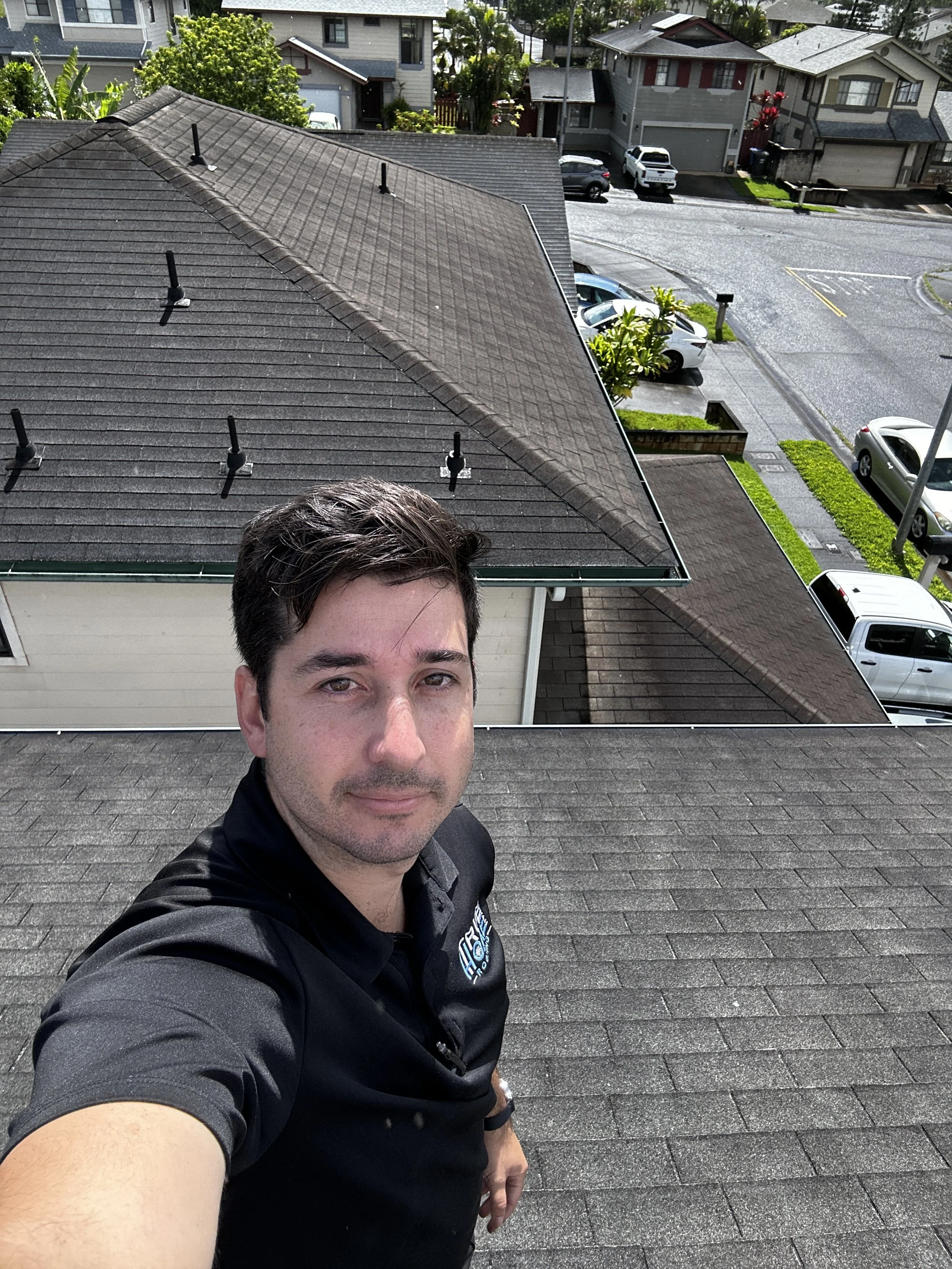 Self-portrait of a man taking a selfie on a rooftop, with a neighborhood street and houses in the background.