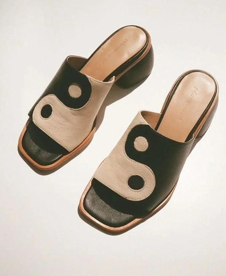 Pair of beige and black slip-on sandals with circular cutouts on the top.