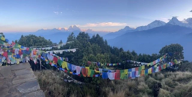 Colorful prayer flags hanging on a hillside with mountain ranges in the background.